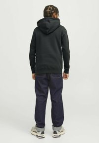 Sudadera negra con capucha y puños acanalados, combinada con jeans sueltos de color azul oscuro y zapatillas claras con acentos grises.