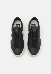 Sneaker in pelle nera con accenti laterali bianchi, punta rotonda e superficie texturizzata. Caratterizzati da lacci neri e una suola chiara.