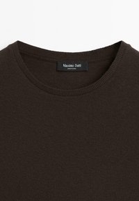 Primo piano di un maglione a girocollo marrone scuro con un'etichetta Massimo Dutti cucita all'interno del collare.