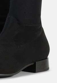 Black ankle boot made of smooth fabric with a slight sheen. Low block heel and minimal stitching details, featuring a rounded toe shape.