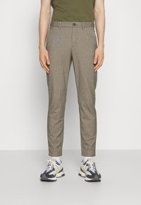 Brązowe spodnie w kratę o dopasowanym kroju, z zapięciem na guzik, bocznymi kieszeniami i gładką fakturą, zestawione z białymi i granatowymi sneakersami.