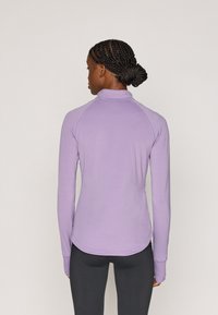 Μακρυμάνικη, ανοιχτόμωβ μπλούζα με ψηλό λαιμό, κατασκευασμένη από απαλό, ελαστικό ύφασμα. Διαθέτει ραγκλάν μανίκια και καμπυλωτή ραφή στο κάτω μέρος.