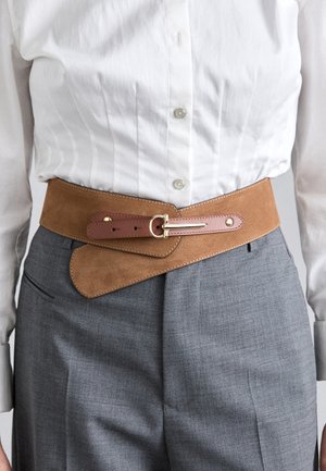 Bruine suède riem met een tan leren gesp, voorzien van een unieke schuine ontwerp, gedragen over grijze maatpakken en een wit shirt.