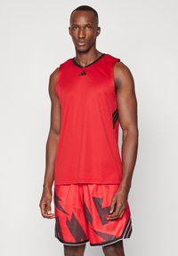 Röd atletisk tanktopp med svarta accents, i kombination med röda shorts som har ett svart abstrakt geometriskt mönster, tillverkade av lätt material.