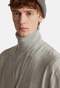 Maglione girocollo grigio con trama a costine, caratterizzato da un design avvolgente e cuciture piatte, abbinato a un cappello di maglia coordinato.