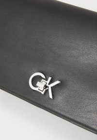 Černá strukturovaná kožená kabelka na psaní s uzávěrem z kovu stříbrné barvy, s hladkým designem a minimalistickým stylem.