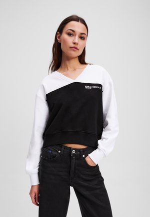 Zwart-witte cropped sweatshirt met een V-hals, voorzien van een diagonale zwarte panel, ribbelboord en een bedrukt logo aan de voorkant.