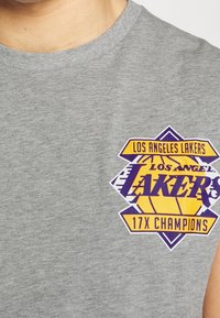 Szara bawełniana koszulka z kolorową grafiką Los Angeles Lakers, zawierającą żółte i fioletowe napisy oraz wzór koszykówki.