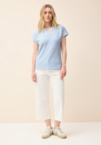 Top de manga corta a rayas azul y blanca con escote en V, combinado con pantalones blancos cortos y zapatillas con acentos azul claro.
