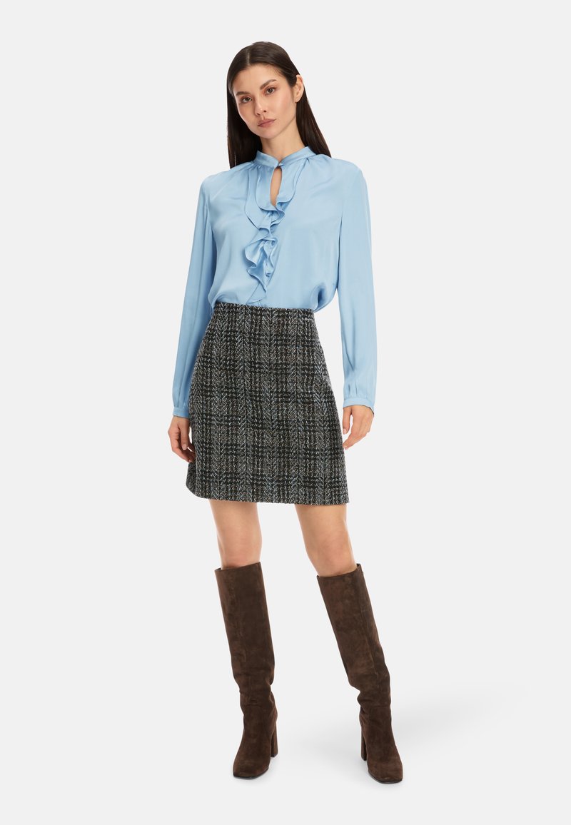 Himmelbluse aus Seide mit Rüschen, kombiniert mit einem schwarz-weißen karierten Rock. Braune Wildlederstiefel bis zum Knie runden das Outfit ab.