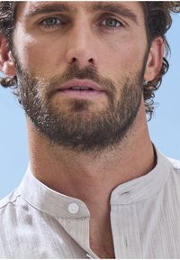 Helles graues, strukturiertes Hemd mit Kragen und Knopfschluss. Mit subtilen Streifen und einem lässigen Schnitt, der die Weichheit des Stoffes betont.