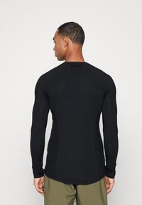 Camisa negra de manga larga hecha de material elástico con diseño ajustado, mangas raglán y dobladillo curvado. Sin logotipos ni patrones visibles.