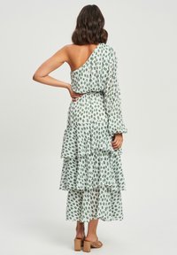 Vestido asimétrico de un solo hombro en blanco con un patrón floral verde; diseño en capas con volantes; tejido ligero; de longitud media; combinado con sandalias marrones.