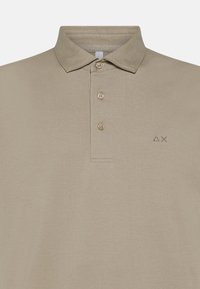 Polo beige realizzato in cotone misto, con colletto classico, tre bottoni e un logo discreto nell'area sinistra del petto.