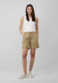 Beige shorts met opgerolde zomen, elastische tailleband en trekkoord. Gepaarde met een witte geribbelde tanktop en lichte sneakers.