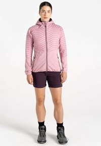 Helle rosa isolierte Jacke mit Kapuze, mit gestepptem Design auf der Brust und den Ärmeln. Getragen über dunklen Shorts und grauen Wanderschuhen.