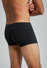 Boxers en coton noirs présentés de dos, avec une taille de largeur moyenne et un ajustement près du corps, mettant en valeur les contours du corps.