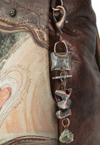 Braune Lederhandtasche mit strukturierter Oberfläche, die einen dekorativen Anhänger mit klaren und metallischen Akzenten sowie detaillierter Stickerei an der Seite aufweist.