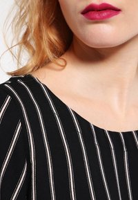 Indumento a righe nere con sottili linee verticali bianche; tessuto morbido; scollatura rotonda; presenta un colore uniforme e liscio nell'area superiore.