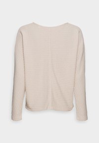 Haut à manches longues beige clair avec une texture à côtes verticales, encolure ronde et coupe décontractée. Détails de couture visibles le long du dos.