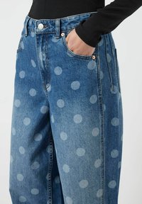 Džínové kalhoty s puntíkovaným vzorem, volného střihu, s pěti kapsami a měděným knoflíkem na pasu. Světle modrá barva.