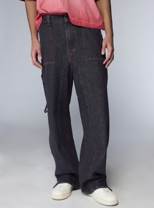 Pantaloni larghi in denim nero con cuciture rosse e grandi tasche, abbinati a scarpe da ginnastica bianche, su uno sfondo neutro.