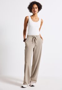 Beige sweatpants with a drawstring waist, side pockets, and black side stripes. Paired with a white sleeveless top and white sneakers.