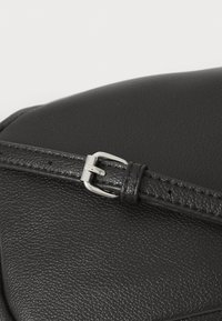 Μαύρη δερμάτινη τσάντα με λεπτομέρειες που περιλαμβάνουν μια ασημένια αγκράφα και ραμμένες λεπτομέρειες, που επιδεικνύει μια υφή στην επιφάνεια και ένα σχεδιασμό ασφαλούς κλεισίματος.