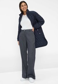 Veste matelassée marine, t-shirt blanc à col rond, pantalon large à rayures et baskets blanches. La veste présente un col haut et une fermeture à pression.