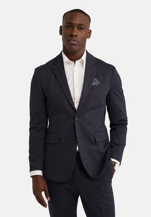Námořnický vlněný oblek se slim fit střihem, s klopami a dvěma předními kapsami, doplněný o kapesníček. V kombinaci s bílou košilí s knoflíky.