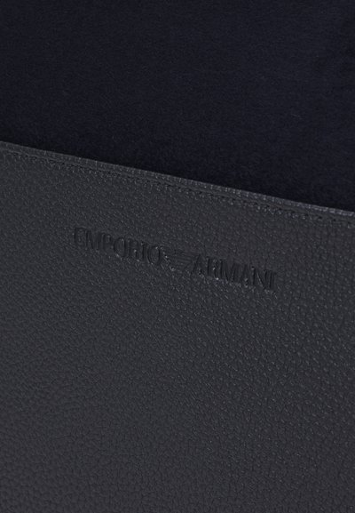 Melns teksturēts ādas mapes ar izspiestu "Emporio Armani" logotipu. Iekšpuse izklāta ar mīkstu melnu audumu. Gluda, minimālisma dizains.