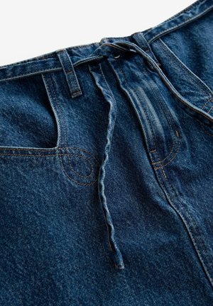 Pantalones de mezclilla con un lavado azul oscuro, que presentan un cinturón de cuerda, costuras decorativas y un diseño clásico de cinco bolsillos.