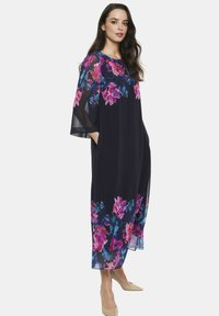 Granatowa maxi sukienka w kwiaty z przezroczystymi rękawami, z dużymi różowymi i niebieskimi wzorami kwiatów. Luźny krój z bocznymi kieszeniami dla wygody.