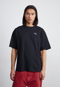 Tricou din bumbac negru cu guler rotund și mâneci scurte; are un mic logo alb Puma în zona stânga a pieptului.