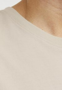 Beige lühikeste varrukatega särk ümmarguse kaelusega, millel on sile, pehme kanga ning kaelaäärel kerge sooniline tekstuur.