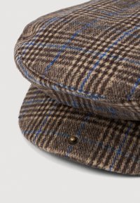 Pruun ja sinine ruuduline villane lame müts ümarate servadega, kõrva küljel on messingist nööp ja pehme tekstuur.