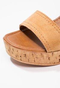 Sandale plateforme en daim beige avec une large bride et une semelle à texture liège, ornée de coutures blanches sur la semelle intérieure.