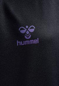 Zwarte stof met een matte textuur met een paarse "hummel" logo met een bijontwerp boven de merknaam, gecentreerd en duidelijk.