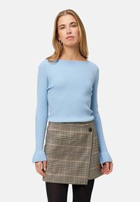 Jasnoniebieski sweter z prążkowanej dzianiny z długimi rękawami, w połączeniu z wężowym spódnicą w kratę z dodatkiem guzików, noszoną na czarnych rajstopach.