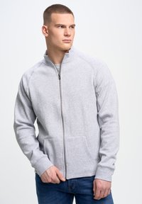 Szara bluza z suwakiem, z wysokim kołnierzem, ściągaczami przy rękawach i dwiema przednimi kieszeniami. Materiał wydaje się gładki i miły w dotyku, odpowiedni do codziennego noszenia.