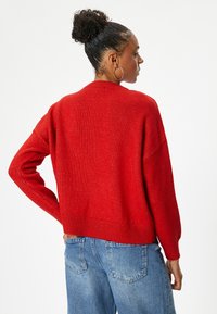 Rode gebreide trui met een ontspannen pasvorm, geribde manchetten en zoom. Draag het met blauwe high-waisted spijkerbroek. Getextureerde stof met een lichte glans.