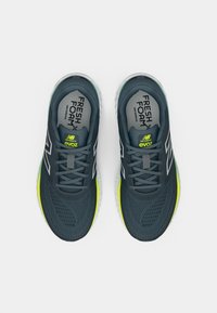 Chaussures de course grises avec tige en mesh respirant, accents réfléchissants et touches vert citron. Équipées de lacets et d'un col rembourré pour le confort.