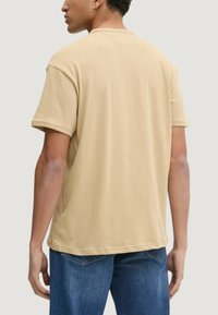 Béžové bavlněné tričko s krátkými rukávy, kulatým výstřihem a zadním V-šitím, kombinované s modrými džínami.