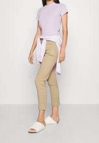 Ljuslila kortärmad t-shirt i kombination med beiga tajta byxor och vita fluffiga tofflor. Outfiten har en knäppt skjorta knuten i midjan.