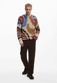 Kleurrijke geribbelde gebreide trui met blauwe, groene, rode en bruine abstracte patronen, gecombineerd met donkergroene cargobroek en sneakers.