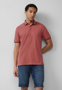 Rožnato polo majico z morsko modrim ovratnikom in rokavi, izdelano iz mehkega blaga, je združeno z modrimi kavbojskimi kratkimi hlačami.