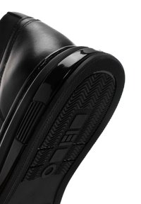Zapato de cuero negro con suela de goma texturizada. Presenta un ribete negro brillante y un patrón zigzagueante prominente en la suela para mayor tracción.