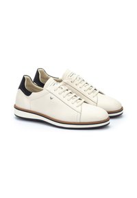 Zapatillas de cuero blanco con un acento negro en el talón, que cuentan con una punta redondeada, un diseño con cordones y una suela de goma texturizada con detalles en marrón.