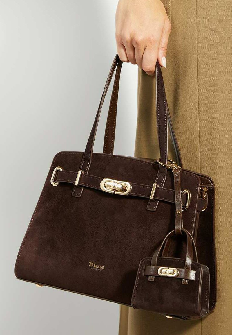 Brown suede handbag with gold hardware, structured design, two top handles, and a smaller detachable bag attached. Logo displayed on the front.