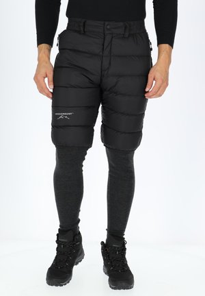 Sorte puffede shorts med en lynlåslomme, der har en tekstureret overflade og en elastisk talje, parret med grå leggings og sorte vandrestøvler.